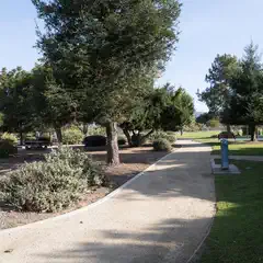 A paved path winds through a park with trees and picnic tables.