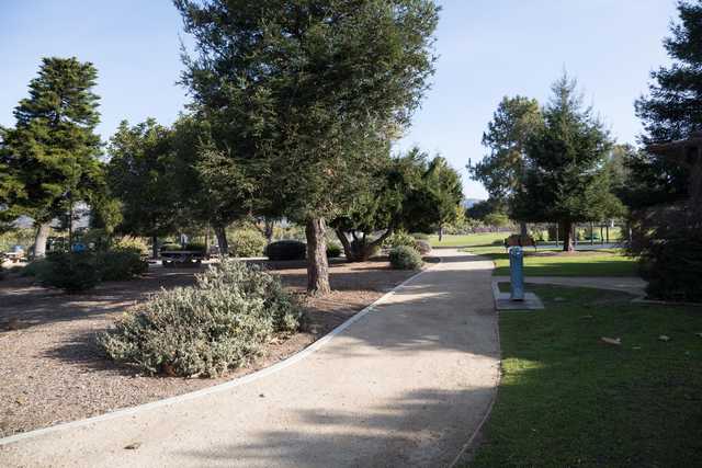 A paved path winds through a park with trees and picnic tables.