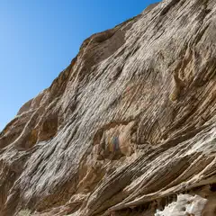 A sandstone cliff face is visible from below, featuring numerous grooves and ridges running vertically down its length.