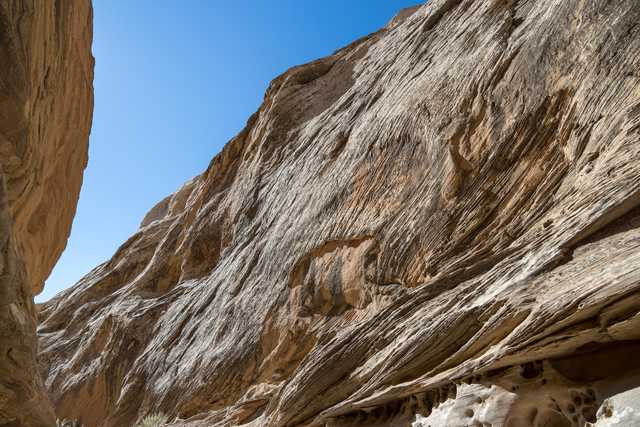 A sandstone cliff face is visible from below, featuring numerous grooves and ridges running vertically down its length.