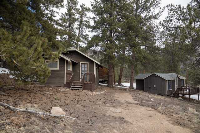 A row of small wooden cabins, each with a porch and steps leading up to it, situated on a rocky hillside surrounded by trees.