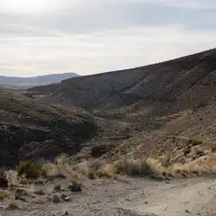 A dirt road winds through a desert canyon flanked by rugged hills and sparse vegetation.