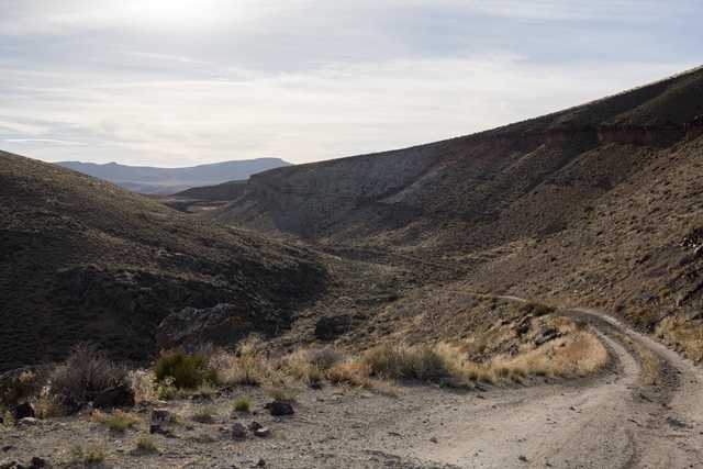 A dirt road winds through a desert canyon flanked by rugged hills and sparse vegetation.