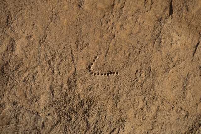 A sandstone cliff face features a line of small, shallow holes at its center.