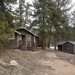 A row of small wooden cabins, each with a porch and steps leading up to it, situated on a rocky hillside surrounded by trees.