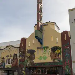 A yellow building features mural paintings of faces and decorative plants.