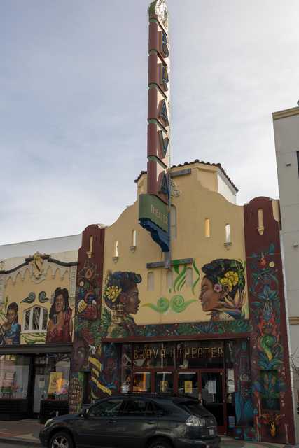 A yellow building features mural paintings of faces and decorative plants.