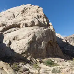 An arid landscape features a large, light-colored rock formation with numerous layers and cracks.