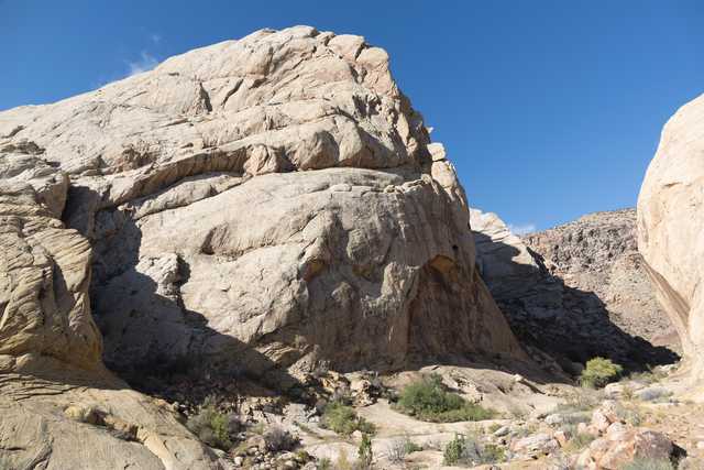 An arid landscape features a large, light-colored rock formation with numerous layers and cracks.