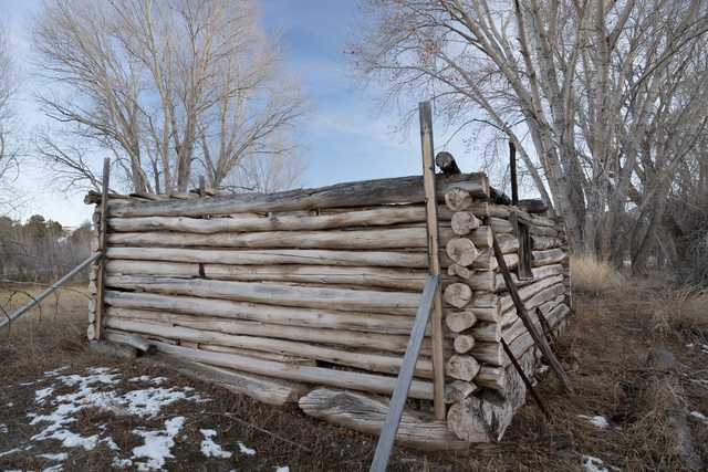 An old, weathered log cabin sitting alone on a snowy ground with bare trees in the background.