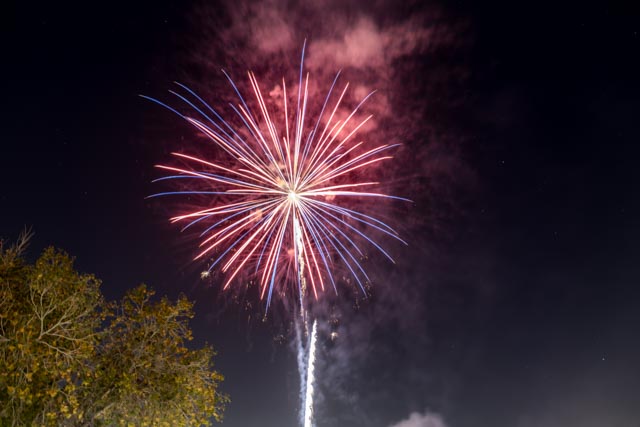 A burst of red, white, and blue fireworks illuminates a dark sky.