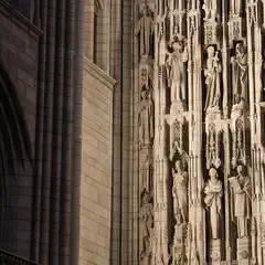 A close-up of a Gothic cathedral facade featuring intricate stone carvings and numerous statues arranged in vertical niches.