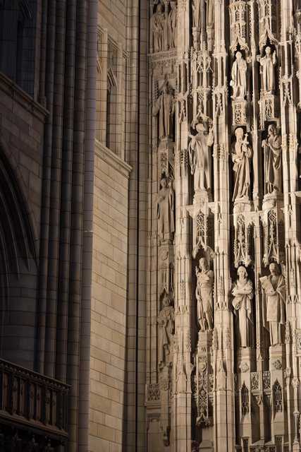 A close-up of a Gothic cathedral facade featuring intricate stone carvings and numerous statues arranged in vertical niches.