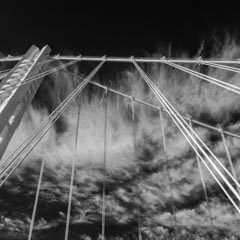 A long suspension bridge with multiple cables against a cloudy sky.