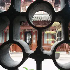A traditional Chinese-style building with intricately carved wooden beams and lattice windows, viewed through a circular metal gate featuring similar designs.