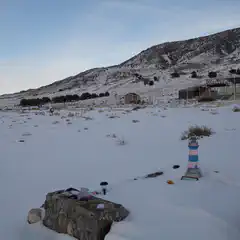 A small, makeshift grave marker set into snow-covered ground against a backdrop of barren trees and distant mountains.
