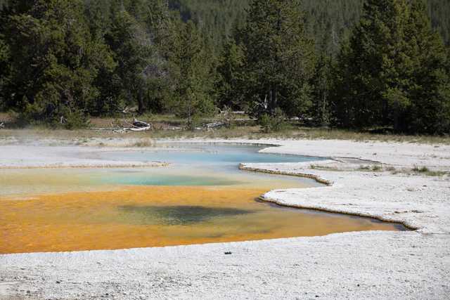 A pool of water is colored yellow and blue, surrounded by white mineral deposits on its edges.