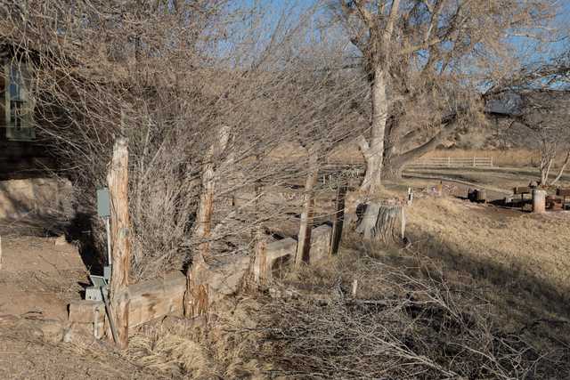 An old wooden fence, leaning and weathered, with bare branches behind it, set against a clear sky.