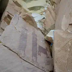 Ancient rock art on a cliff face, featuring animal figures and human-like shapes.
