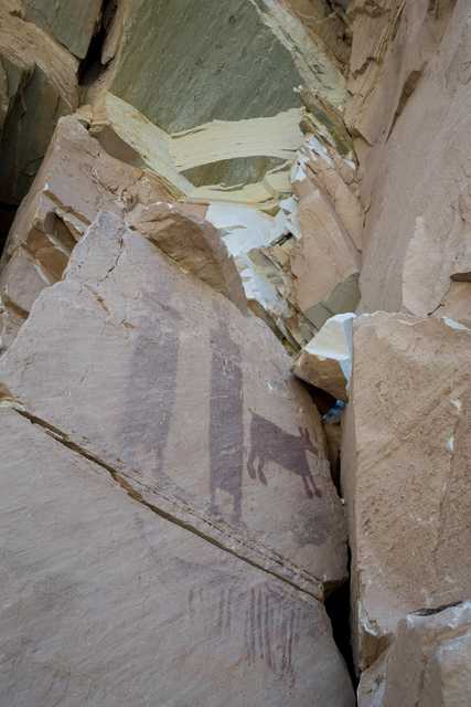 Ancient rock art on a cliff face, featuring animal figures and human-like shapes.