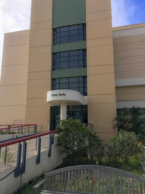 A multi-story building has a green section on the upper level and a white entryway with a curved sign above the doors.