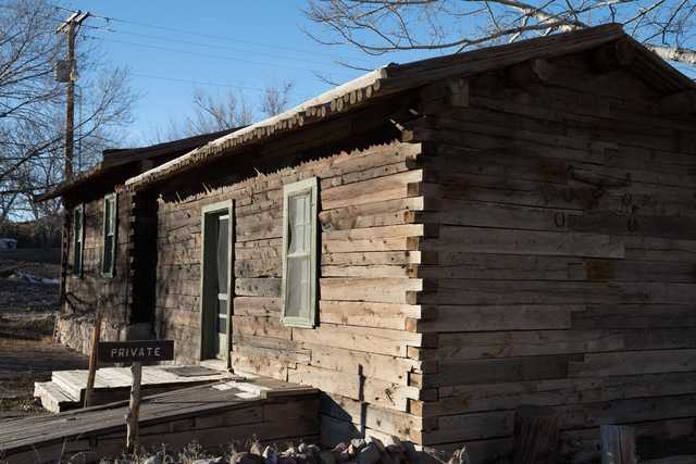 A weathered wooden cabin with a green door and window frames, set against a clear sky.