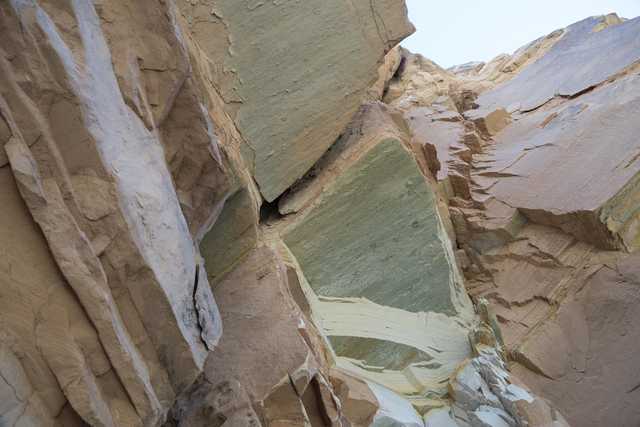 A rocky cliff face with jagged edges, showing layers and cracks in various shades of brown, tan, and green.