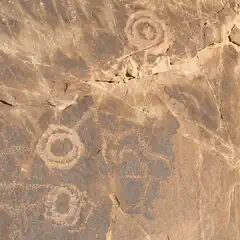 A rock with petroglyphs of concentric circles and other abstract designs carved into its surface.