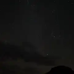 A green streak is visible against a starry sky over a mountainous landscape.
