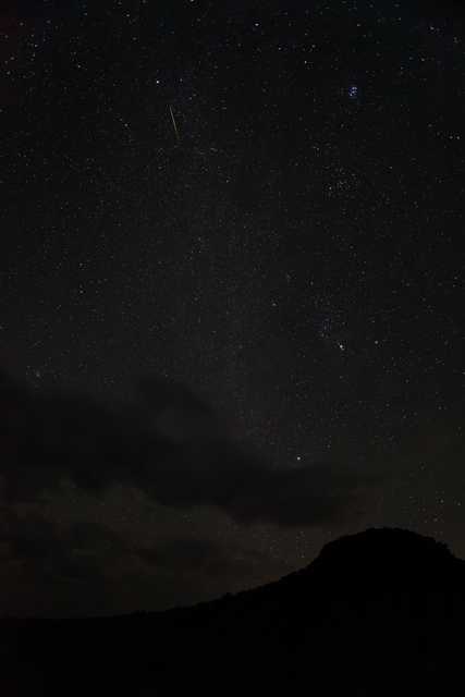 A green streak is visible against a starry sky over a mountainous landscape.