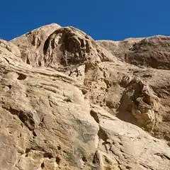 A rocky outcropping made of light-colored rock has several holes and grooves on its surface.
