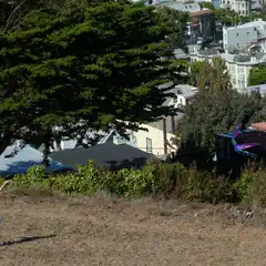 A boy is running across a hillside, holding a kite string in his right hand.