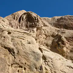 A rocky outcropping made of light-colored rock has several holes and grooves on its surface.