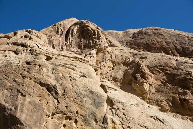 A rocky outcropping made of light-colored rock has several holes and grooves on its surface.