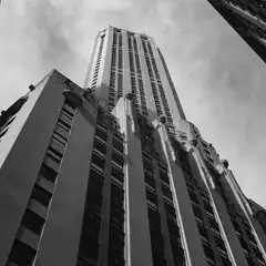 A tall building occupies the majority of the frame, flanked by portions of adjacent structures and a cloudy sky.