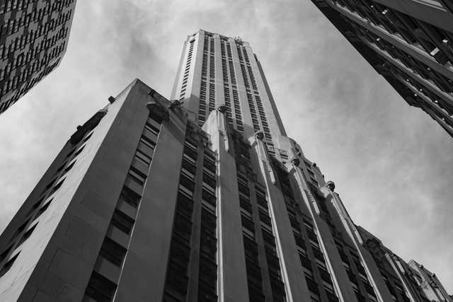 A tall building occupies the majority of the frame, flanked by portions of adjacent structures and a cloudy sky.