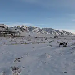 A snowy landscape with mountains in the background and small gravesites covered in snow.