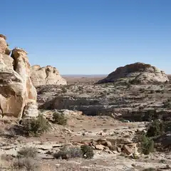A rocky outcropping rises from a desert landscape, composed of light-colored rock with visible layers and striations.