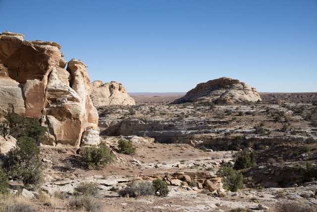 A rocky outcropping rises from a desert landscape, composed of light-colored rock with visible layers and striations.