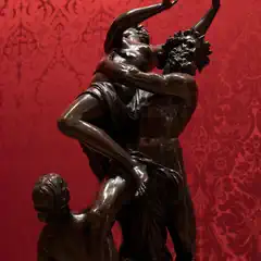 A sculpture depicting three figures with dynamic poses and intense expressions, set against a red background.