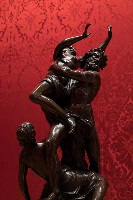 A sculpture depicting three figures with dynamic poses and intense expressions, set against a red background.