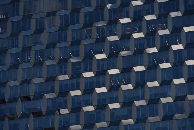 A facade of a building covered in blue-tinted glass panels arranged in a geometric pattern.