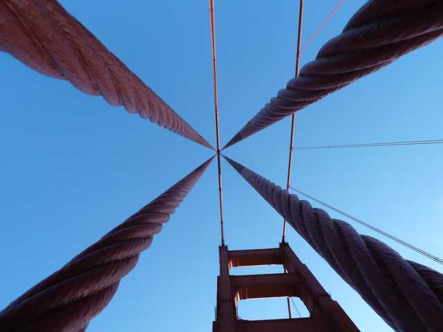 A close-up view of a bridge's suspension cables against a clear blue sky.