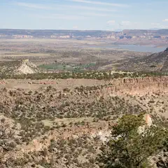 A rugged, rocky landscape with sparse vegetation extends towards distant canyons and a body of water.