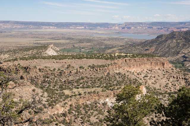 A rugged, rocky landscape with sparse vegetation extends towards distant canyons and a body of water.