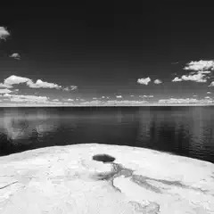 A large rock formation juts out into a calm body of water under a partly cloudy sky.