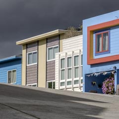 A row of colorful houses on a hillside, with dark clouds above and a concrete road below.