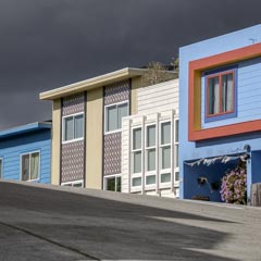 A row of colorful houses on a hillside, with dark clouds above and a concrete road below.