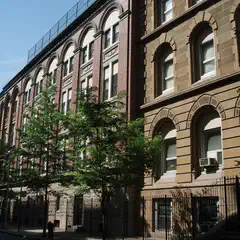 A row of tall buildings with arched windows and decorative stonework lines a street.