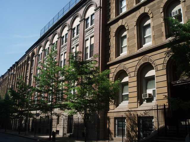 A row of tall buildings with arched windows and decorative stonework lines a street.